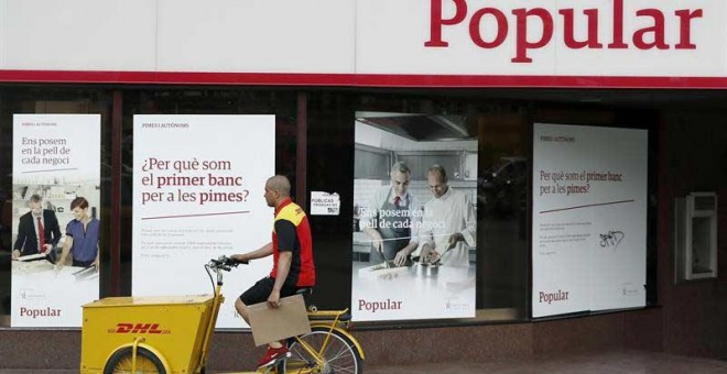 Un repartidor pasa ante una oficina del Banco Popular en el Paseo de Gracia esquina con la calle Aragón de Barcelona. | ANDREU DALMAU (EFE)