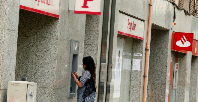 Una mujer saca dinero en un cajero de una entidad del Banco Popular que si sitúa junto a otra del banco Santander.REUTERS/Albert Gea