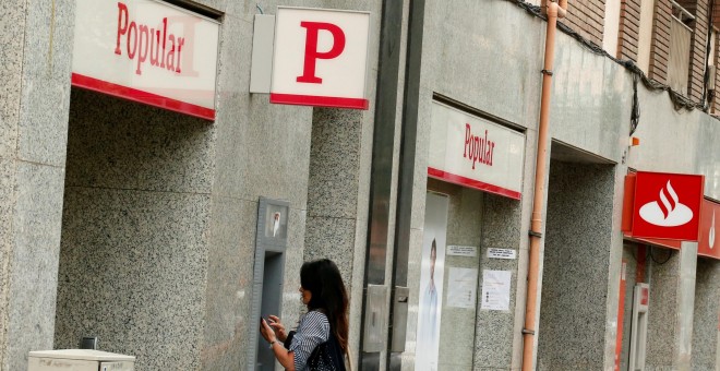 Una mujer saca dinero en un cajero de una entidad del Banco Popular que si sitúa junto a otra del banco Santander.REUTERS/Albert Gea