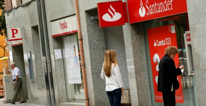 Un par de personas utilizan un cajero automático de una oficina del Banco Santander, en Barcelona, situada junto a una sucursal del Popular. REUTERS/Albert Gea