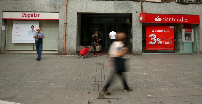 Varios personas pasan junto a sendas oficinas de Banco Popular y Banco Santander, en Barcelona. REUTERS/Albert Gea