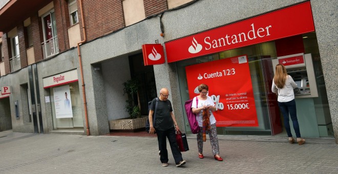 Una mujer utiliza el cajero automático de una oficina del Banco Santander, ubicado junto a un sucursal del Banco Popular, en Barcelona. REUTERS/Albert Gea