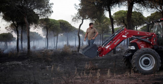 Un hombre se monta en un tractor mientras ayuda a apagar el incendio forestal cerca del Parque Nacional de Donaña en Mazagón. REUTERS/Jon Nazca