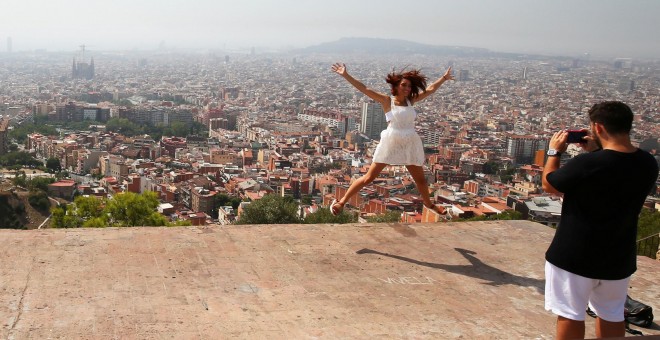 Una joven turista salta,mientras le toman una foto con el 'skyline' de Barcelona a su fondo. REUTERS/Albert Gea