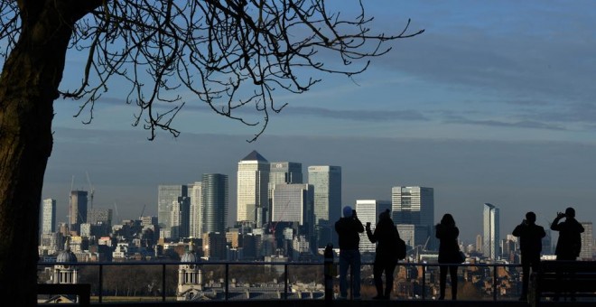 Varias personas toman fotos desde el Parque Greenwich de Canary Wharf, el distrito financiero londinense donde tienen su sede gran número de bancos internacionales y oficinas. AFP/Ben Stansall