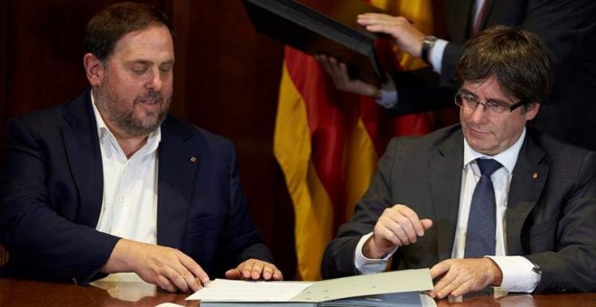 El presidente de la Generalitat, Carles Puigdemont (derecha), acompañado por el vicepresidente Oriol Junqueras, firma la convocatoria de referéndum. | ALEJANDRO GARCÍA (EFE)