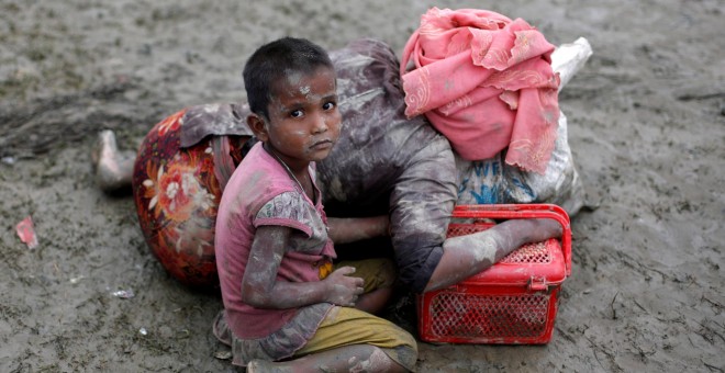 Una nia ronhiny sentada junto a su madre, que descansa tras cruzar la frontera entre Brimania y Bangladesh. - REUTERS