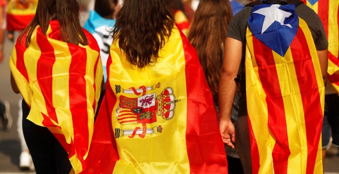 Tres jóvenes caminan por barcelona con la senyera, la bandera de España y la estelada.- REUTERS