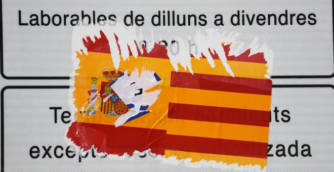 Una pegatina con la bandera española y la senyera, rasgada en un cartel Barcelona. REUTERS