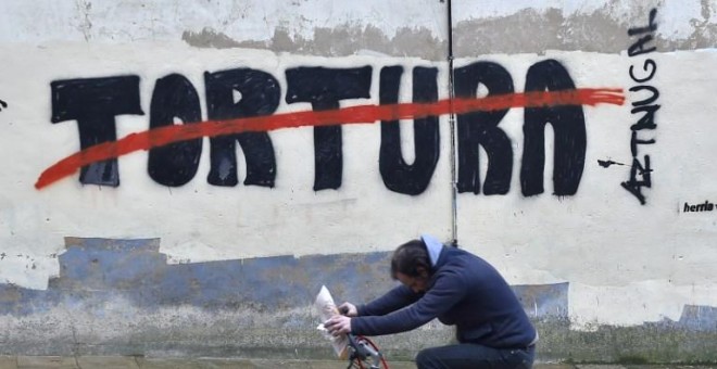 Un hombre pasea en bicicleta por un graffiti contra la tortura en el pueblo vasco de Agurain / Salvatierra. ANDER GILLENEA / AFP