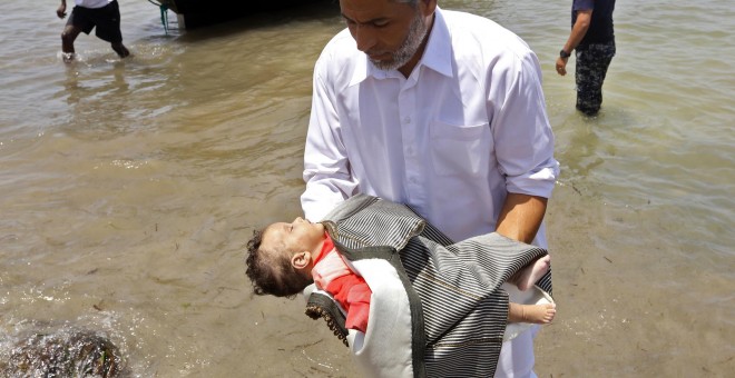 Guardacostas libios sostienen los cadáveres de tres bebés fallecidos en el naufragio frente a las costas libias. Hay cien desaparecidos y 16 supervivientes.- AFP/ MAHMUD TURKIA