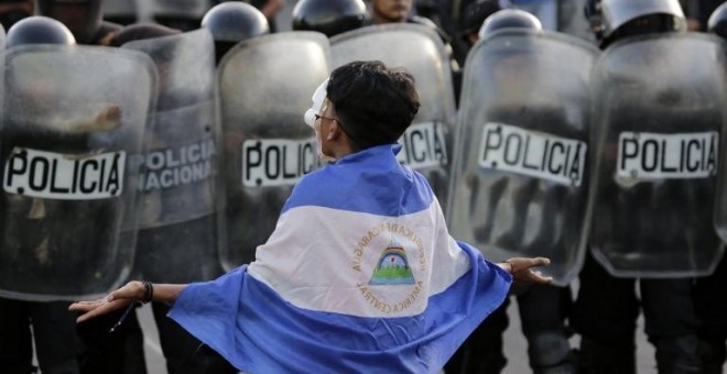 Un joven enmascarado protesta contra el gobierno del presidente nicaragüense, Daniel Ortega, frente a una línea de policías antidisturbios. / AFP - INTI OCON