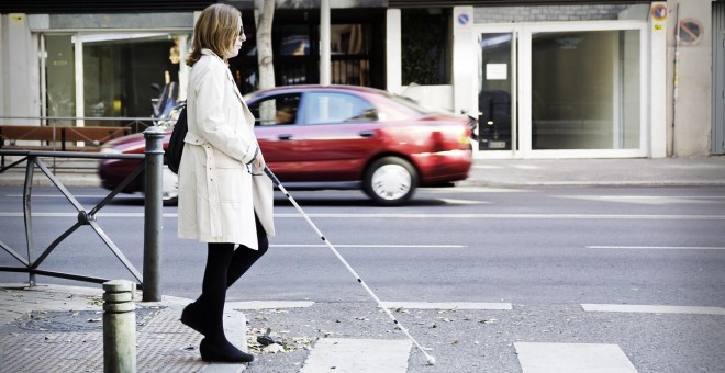 Una persona con discapacidad visual cruzando un paso de peatones ayudándose con un bastón. / ONCE