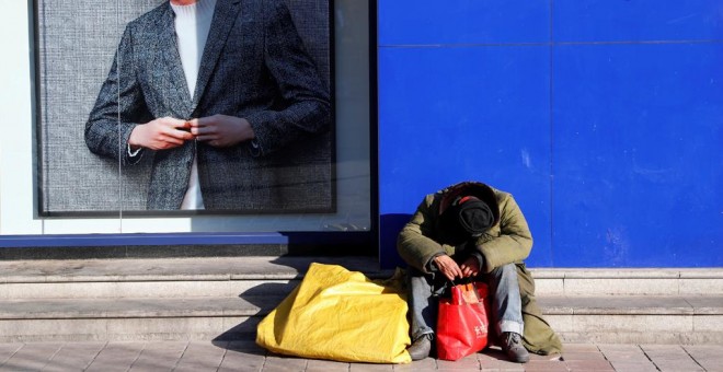 Un sintecho descansa junto al escaparate de una tienda en una calle en Pekín (China). EFE/ Wu Hong