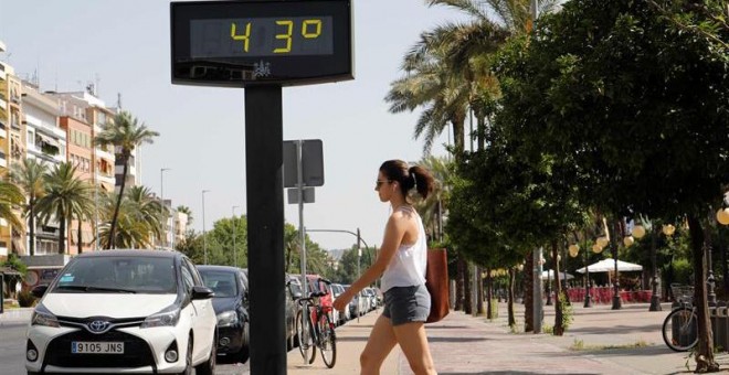Una mujer camina junto a un termómetro que marca 43 grados en las calles de Córdoba. - EFE
