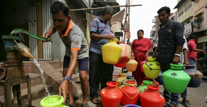 Un hombre usa una bomba manual para llenar un recipiente con agua potable mientras otros esperan en una cola en una calle de Chennai./ REUTERS