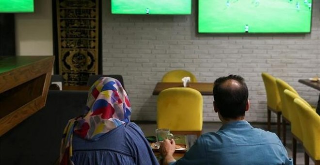 Una mujer ve un partido de fútbol junto a un amigo en una cafetería de Irán. REUTERS