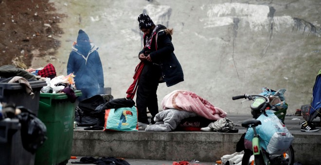 Los migrantes recogen sus pertenencias tras ser desalojados por la policía. / Reuters