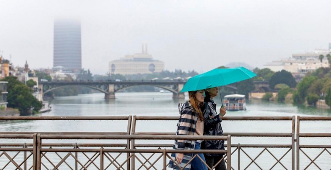 17/11/2019.- Dos personas atraviesan el puente de San Telmo en un día de lluvia en Sevilla. / EFE - JULIO MUÑOZ