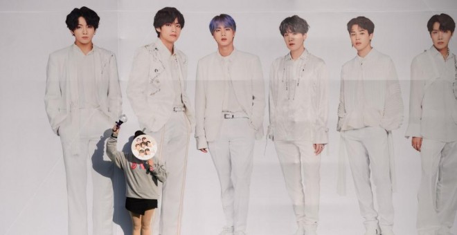 Una fan del grupo coreano de k-pop BTS posa junto a un cartel con los miembros de la banda. - AFP