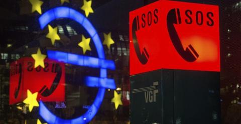 Fotografía que muestra el símbolo del Euro reflejado en una ventana junto al letrero luminoso de un teléfono de emergencia, en Fráncfort, Alemania. EFE