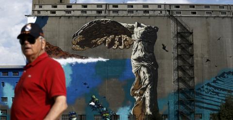 Un hombre pasa por delante de una pintada que reproduce la estatuta de la Vcotira de Samotracia, cerca del puerto del Pireo, en Atenas. REUTERS/Alkis Konstantinidis