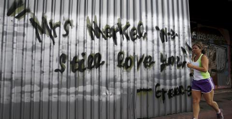 Una mujer corriendo por las calles de Atenas, pasa junto a una pintada que, en inglés, dice 'Señora Merkel, todavía la queremos. Grecia'. REUTERS/Alkis Konstantinidis
