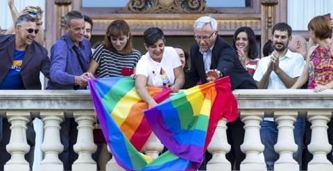 El alcalde de Valencia, Joan Ribó (centro), despliega desde el balcón del Ayuntamiento la bandera arco iris con motivo del Día Internacional del colectivo LGTB. /EFE