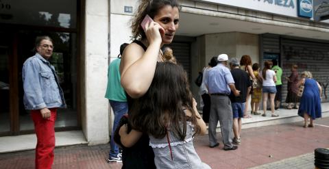 Una niña se abraza a su madre junto a una cola de ciudadanos griegos que esperan para sacar dinero de un cajero en Atenas. REUTERS/Alkis Konstantinidis