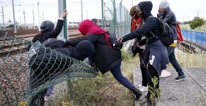 nmigrantes cruzan una valla al tratar de llegar al tren que los conduciría a Inglaterra. EFE