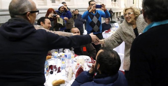 La alcaldesa de Madrid, Manuela Carmena (d), saluda a algunas de las 200 personas sin hogar que esta noche cenan en el Palacio de Cibeles, organizadas por la Fundación Mensajeros de la Paz que preside el padre Ángel en colaboración con el Ayuntamiento de