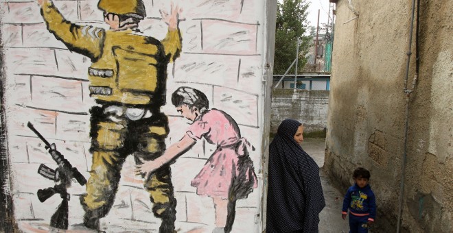 Una mujer palestina se encuentra con un niño en un callejón junto a la reproducción de un mural del artista callejero británico Banksy en al-Aroub campo de refugiados palestinos, al norte de la ciudad cisjordana de Hebrón. HAZEM BADER/AFP