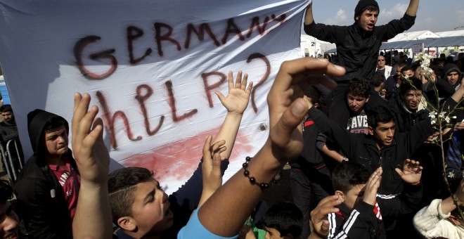 Refugiados e inmigrantes agitan una bandera y gritan consignas durante una protesta en la frontera entre Grecia y Macedonia, reclamando ayuda. REUTERS