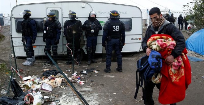 Un hombre recoge sus pertenencias ante la mirada de los agentes antidisturbios desplegados en la 'Jungla'. - EFE