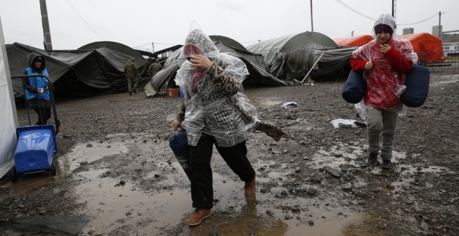 Varias personas tratan de protegerse de la lluvia en una de las tiendas del campamento de Slavonski Brod. - REUTERS