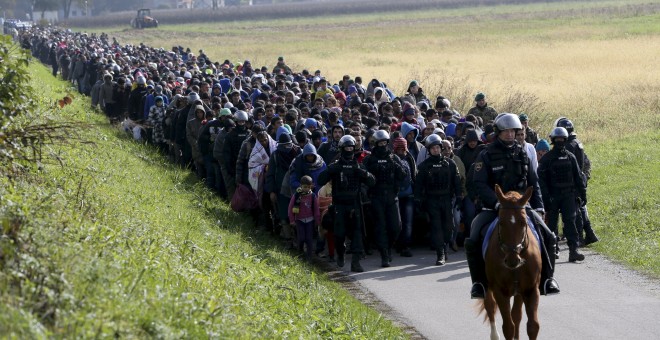 Un policía guía a un grupo de refugiados hacia la entrada del campo de Dovoba, en Eslovenia./ REUTERS