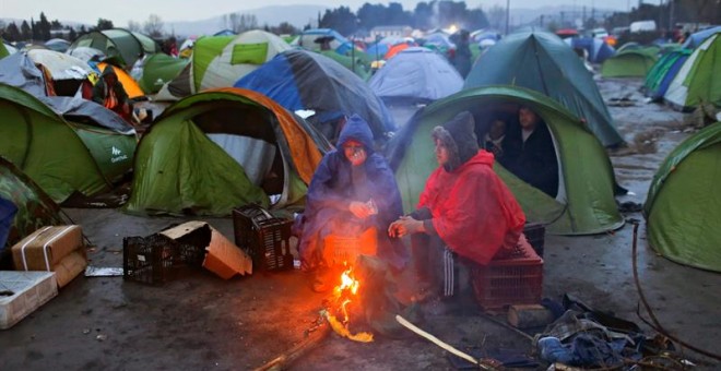 Varios refugiados se calientan junto al fuego entre sus tiendas de campaña en un campamento de refugiados en la frontera entre Grecia y Macedonia.- Valdrin Xhemaj (EFE)