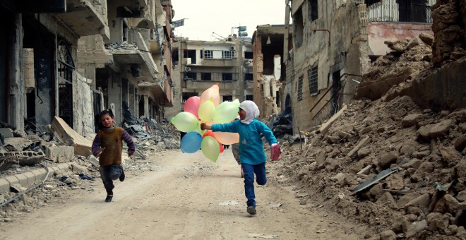Niños sirios juegan con globos entre edificios dañados en el barrio de Jobar, a las afueras de la capital siria de Damasco. AMER ALMOHIBANY / AFP