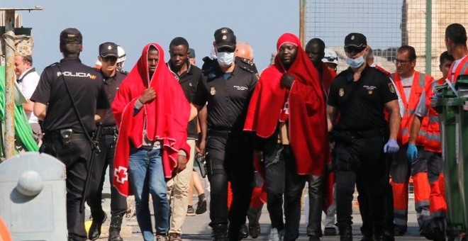 Efectivos de la Policía y miembros de Cruz Roja con varios de los 24 inmigrante, 22 hombres y dos mujeres, de origen subsahariano que han llegado al puerto de Almería.  EFE / Carlos Barba