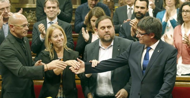El presidente de la Generalitat, Carles Puigdemont, saluda a los consellers Neus Munté y Raül Romeva en el pleno del Parlament. - EFE