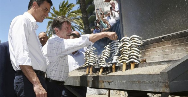 El líder del PSOE y candidato a la presidencia del Gobierno, Pedro Sánchez, escucha las explicaciones del espetero Vicente Padilla, en Marbella, de cómo deben ensartarse las sardinas en las cañas para evitar que se caigan y se quemen, tras reunirse hoy co