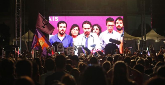 Simpatizantes de Unidos Podemos escuchan las declaraciones de su líder Pablo Iglesias (c. en la pantalla) durante su comparecencia ante la prensa tras conocer los resultados de las elecciones generales celebradas en España, hoy en la plaza del museo Reina