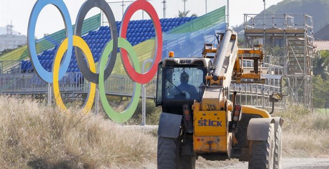 Un vehículo de construcción pasa cerca de unos anilllos olímpicos en una instalación en Barra de Tijuca. /EFE