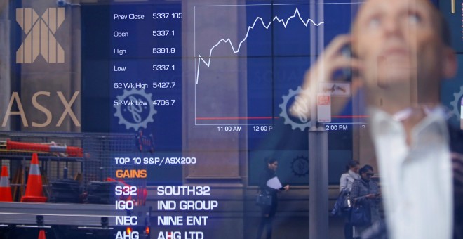 Un inversor habla con su móvil junto a un monitor con información sobre la bolsa australiana, en Sydney. REUTERS/Steven Saphore