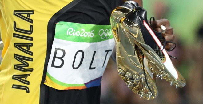 El atleta jamaicano Usain Bolt con sus zapatilas en la mano tras vencer en la carrera de 100 metros en los JJOO de Río. REUTERS/Phil Noble