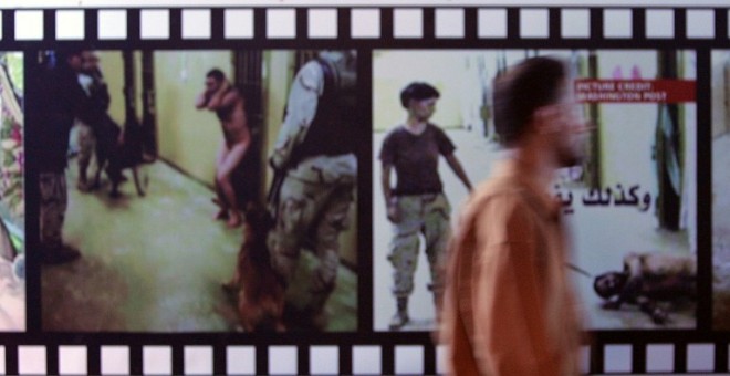 Un iraquí junto a unos paneles que muestran fotografías sacadas de la prisión de Abu Ghraib, gestionada por EEUU y donde los militares estadounidenses abusaban de los presos. - AFP
