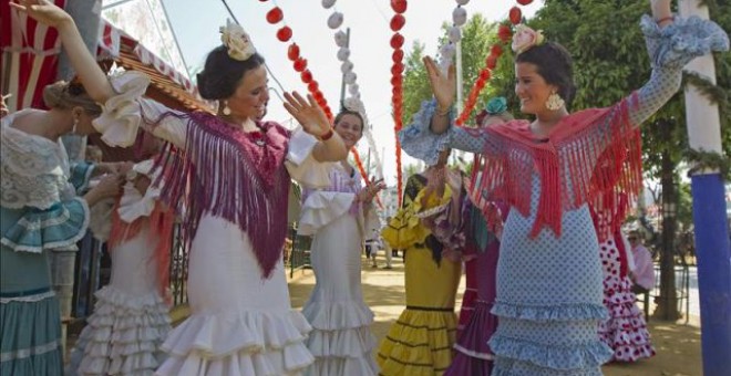 Jóvenes vestidas con el traje típico de flamenca bailan sevillanas en el Real de la Feria de Abril de la capital hispalense. EFE/Archivo