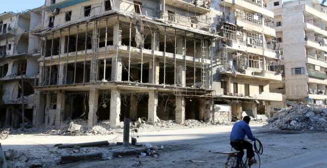 Un hombre pasa en bicicleta por un edificio destrozado por las bombas en Alepo. /REUTERS