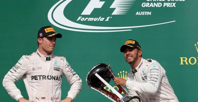 Lewis Hamilton levanta el trofeo de ganador del GP de EEUU ante la mirada de Rosberg. /REUTERS