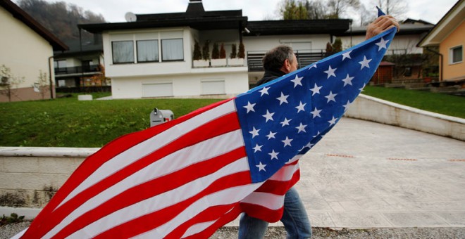 Un hombre ondea una bandera de Estados Unidos delante de la casa de los padres de Melania Trump. / SRDJAN ZIVULOVIC